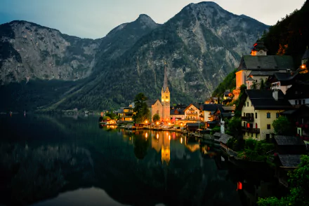 4K Ultra HD wallpaper of Hallstatt village in Austria, showcasing houses and a church reflected on a serene lake with towering mountains in the background at dusk.