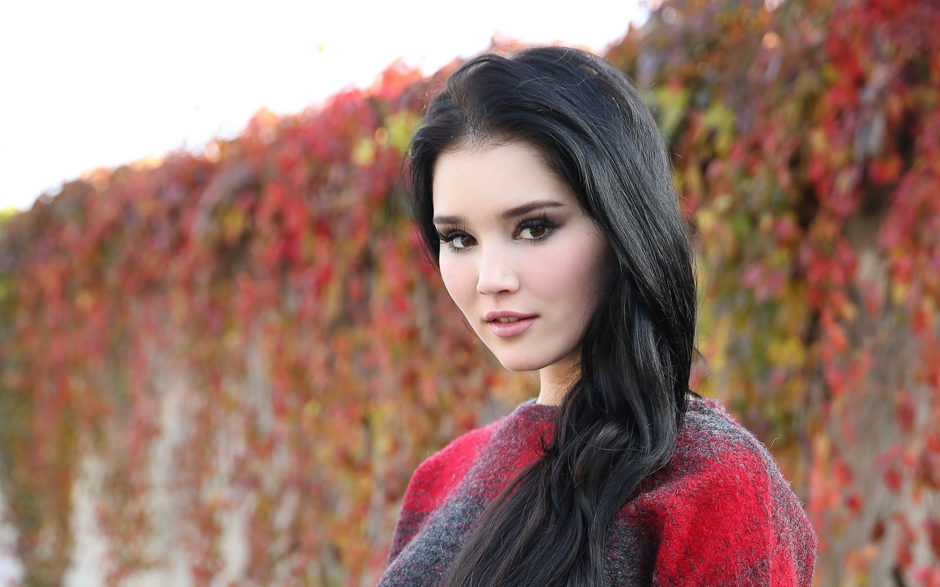 HD desktop wallpaper featuring a brunette woman with brown eyes, posing outdoors against a backdrop of vibrant fall foliage.