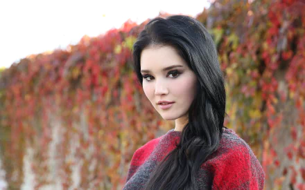 HD desktop wallpaper featuring a brunette woman with brown eyes, posing outdoors against a backdrop of vibrant fall foliage.