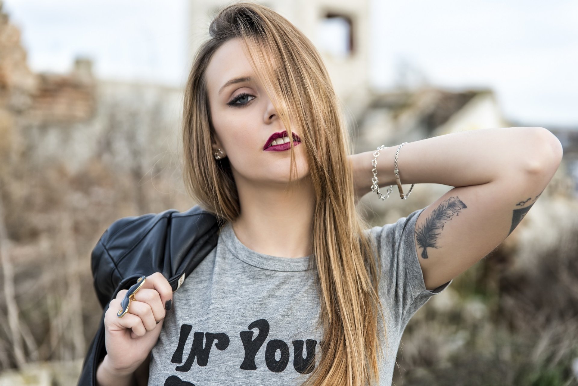 HD PC desktop wallpaper of a blonde woman model with blue eyes and bold lipstick, wearing a leather jacket and showing an arm tattoo.
