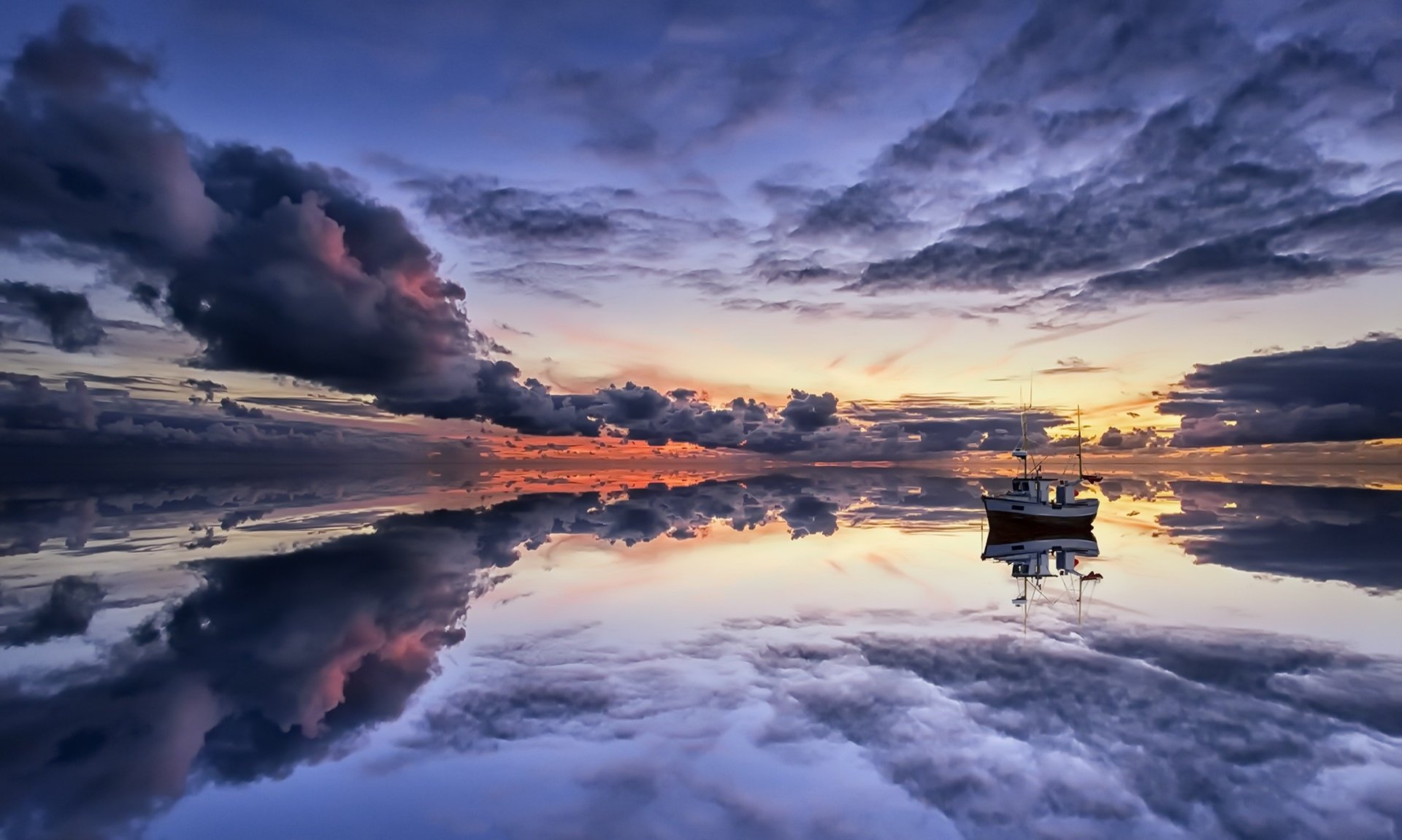 Fishing boat floats peacefully on a calm ocean at sunset, with dramatic clouds and sky perfectly reflected on the water, creating a serene horizon scene.