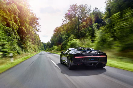Black Bugatti Chiron captured in motion blur speeding down a forest-lined road, featuring dynamic movement in this HD desktop wallpaper background.