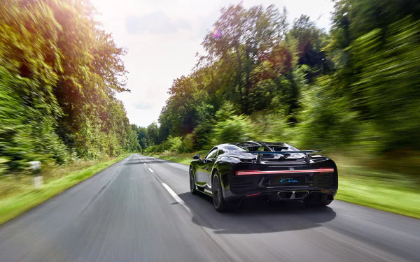 Black Bugatti Chiron captured in motion blur speeding down a forest-lined road, featuring dynamic movement in this HD desktop wallpaper background.