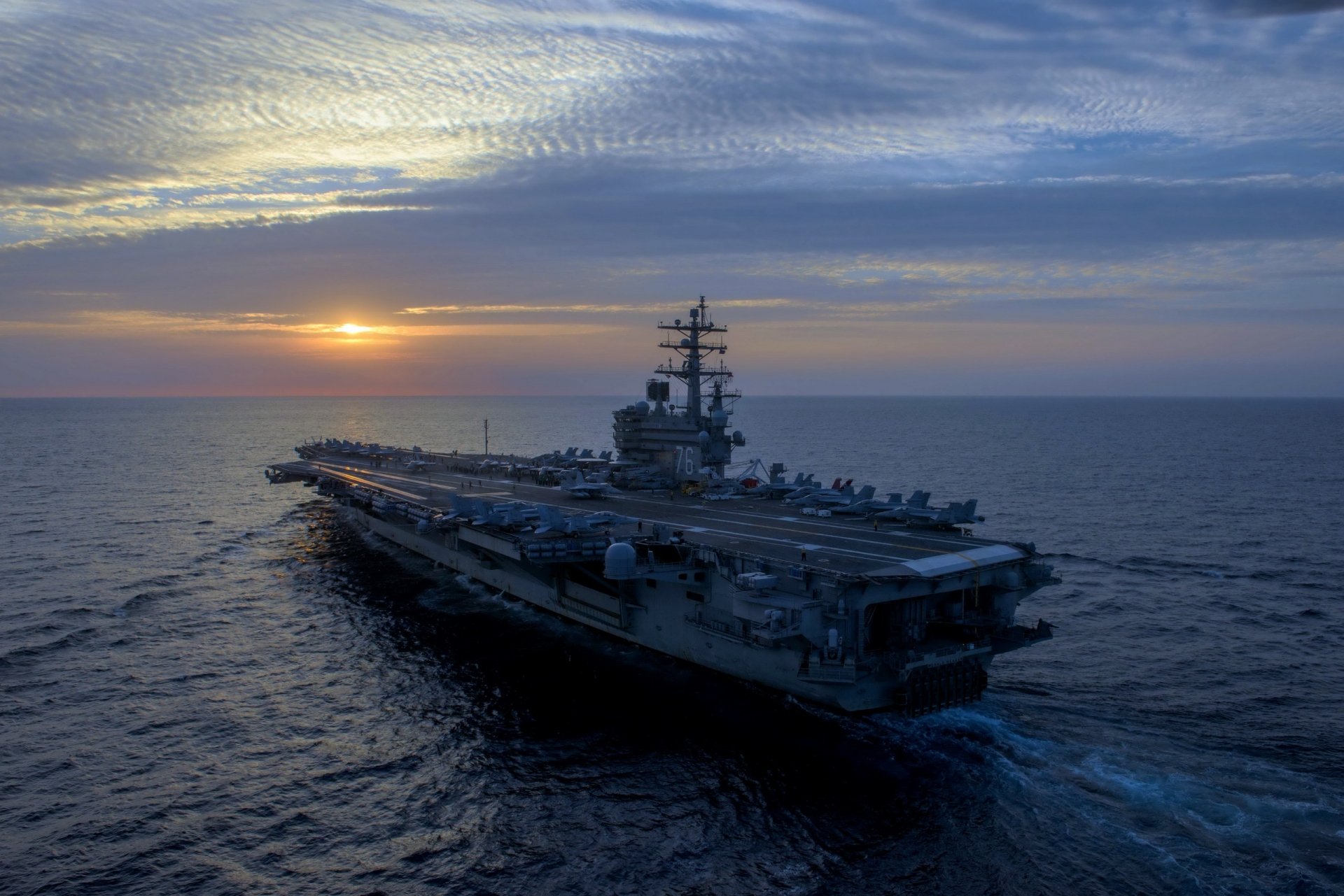 A striking HD desktop wallpaper featuring the USS Ronald Reagan (CVN-76) aircraft carrier sailing into the sunset, showcasing its impressive military presence at sea.