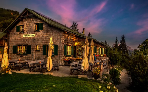 Sunset over a man-made hotel nestled in the Austrian Alps, with warm wooden architecture and closed umbrellas against a colorful evening sky.