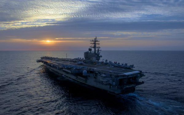 A striking HD desktop wallpaper featuring the USS Ronald Reagan (CVN-76) aircraft carrier sailing into the sunset, showcasing its impressive military presence at sea.