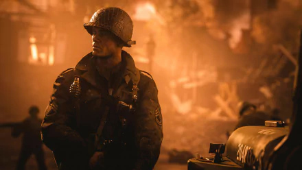 A soldier in WWII uniform stands amidst a fiery battlefield in this HD desktop wallpaper from Call of Duty: WWII.