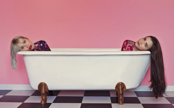 HD PC desktop wallpaper and background: two models — a blonde and a brunette wearing lipstick — lean over a white clawfoot bathtub against a pink wall and checkerboard floor.