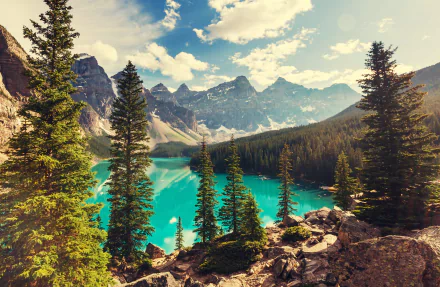 Moraine Lake in Banff National Park, Canada, showcases turquoise water surrounded by evergreen trees, forest, and rugged mountain peaks under a partly cloudy sky.