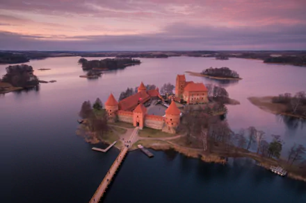Aerial view of Trakai Island Castle surrounded by lake waters at horizon during sunset in Lithuania, captured as an HD PC desktop wallpaper and background.