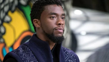 HD desktop wallpaper featuring Chadwick Boseman as Black Panther. He is wearing a dark, patterned garment with a colorful background.