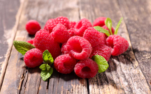 Close-up of fresh raspberries with green mint leaves on rustic wooden surface, captured in 8K Ultra HD for PC desktop wallpaper and background.