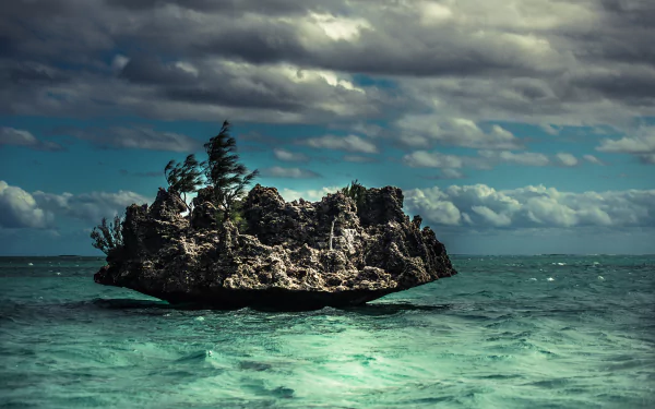 HD desktop wallpaper featuring a seascape with waves crashing against a rocky outcrop. The ocean is vibrant under a cloudy sky with wind-blown trees on the rock and calm sea around.
