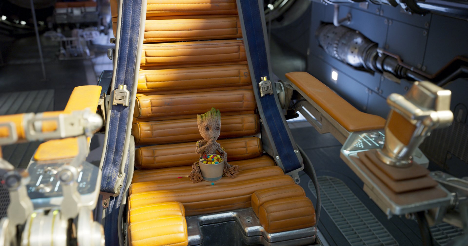 HD desktop wallpaper featuring Baby Groot from Guardians of the Galaxy Vol. 2, sitting on an orange cushioned chair in a futuristic setting.