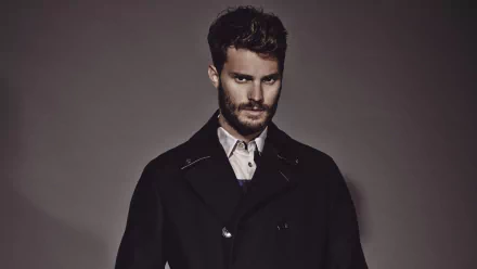 A striking HD desktop wallpaper featuring celebrity Jamie Dornan, showcasing his stylish look with a beard and a dark coat against a neutral background.