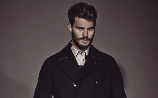 A striking HD desktop wallpaper featuring celebrity Jamie Dornan, showcasing his stylish look with a beard and a dark coat against a neutral background.