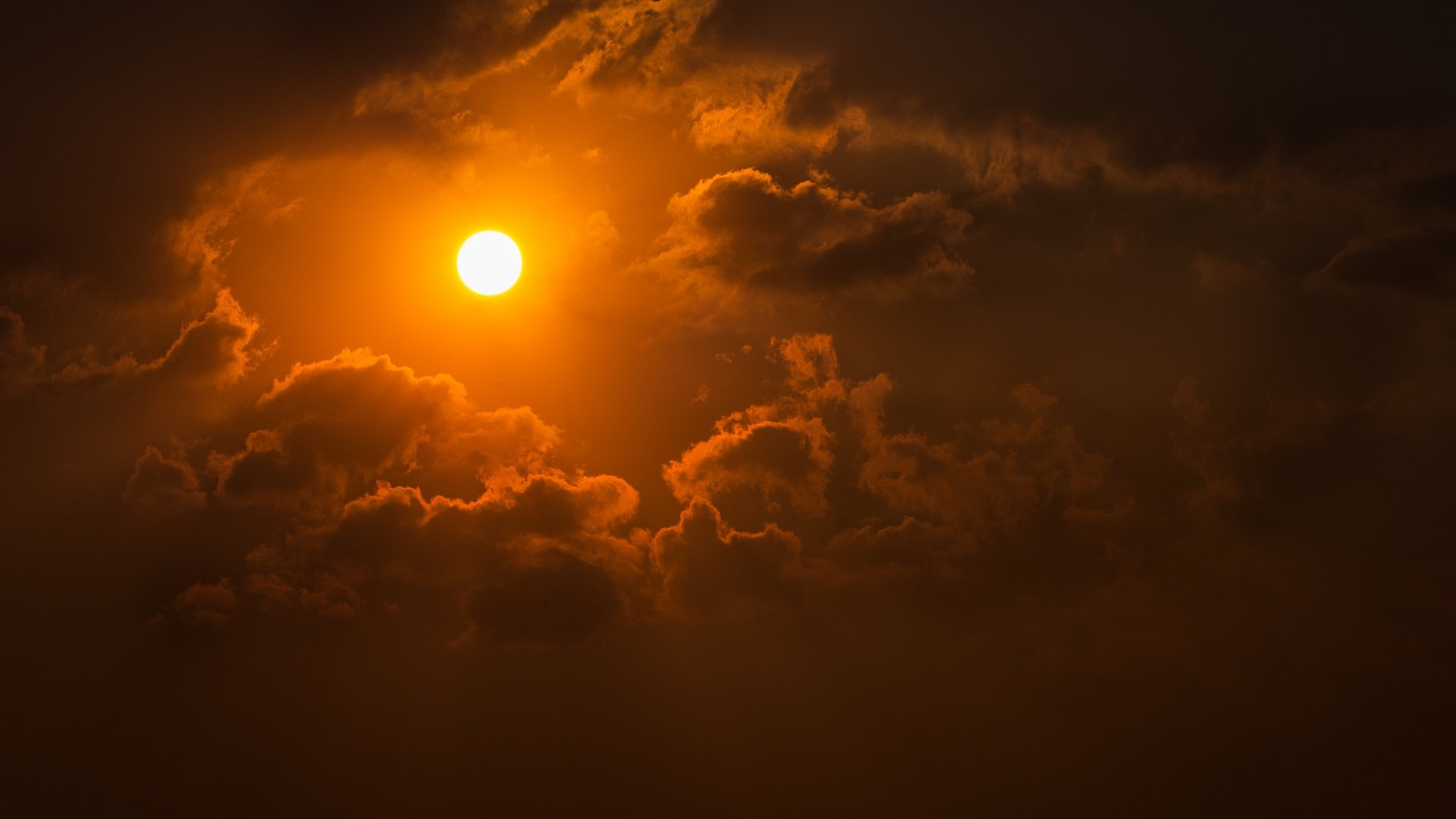 4K Ultra HD desktop wallpaper featuring a vibrant sunset with the sun glowing through dramatic clouds over a natural landscape.