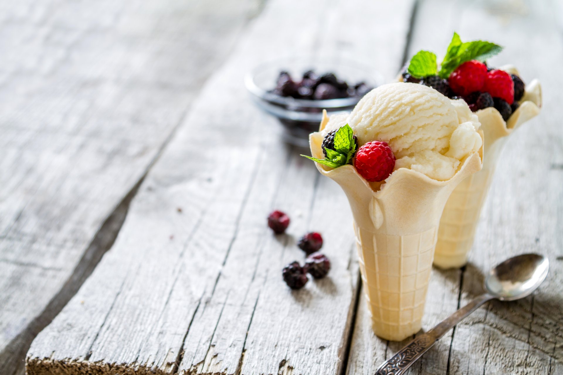 4K Ultra HD still life of creamy ice cream scoops served in waffle cones, garnished with fresh berries and mint leaves on a rustic wooden surface.