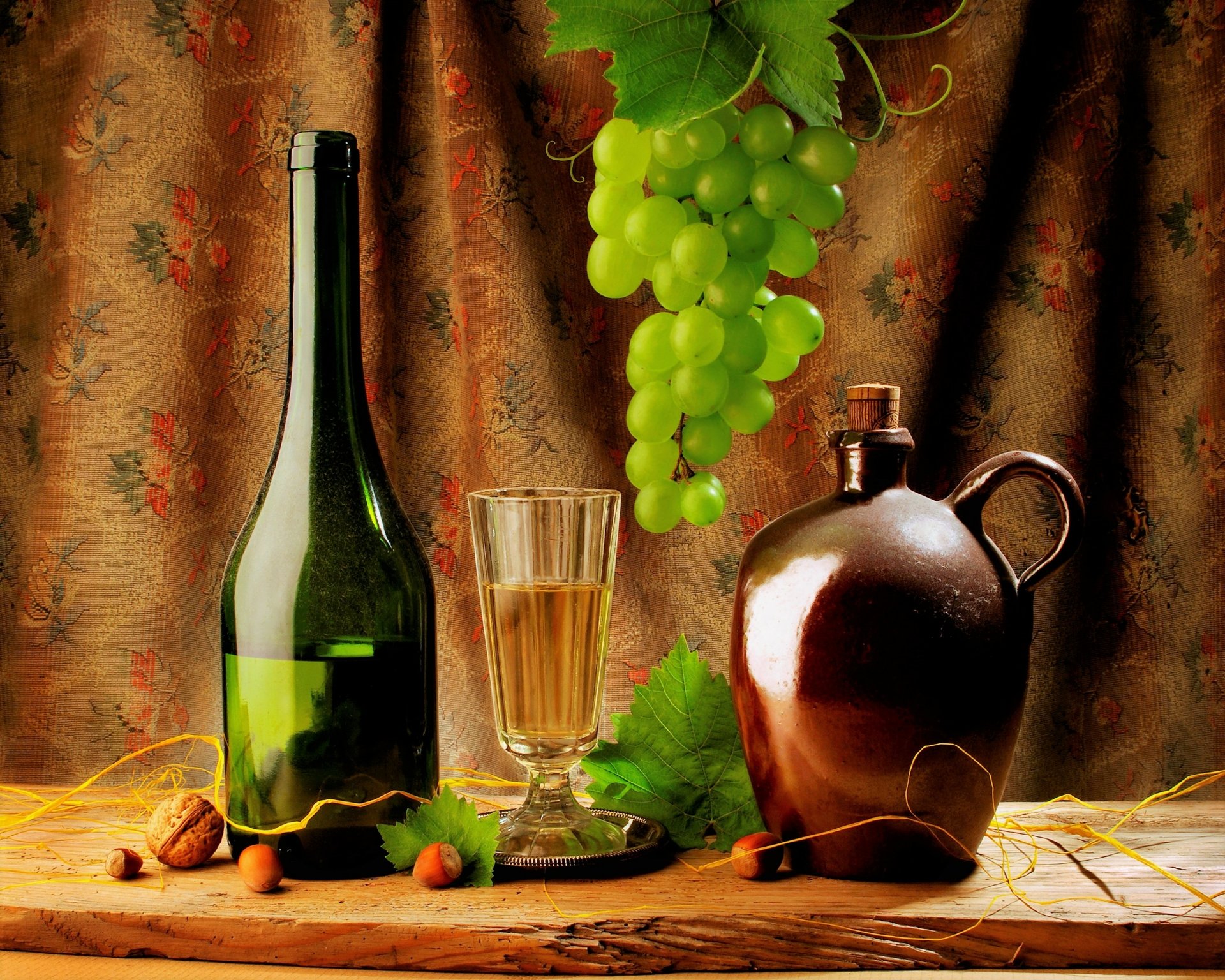 HD still life desktop wallpaper featuring a green wine bottle, glass, cluster of green grapes, a brown jug, and grape leaves against a textured fabric backdrop.
