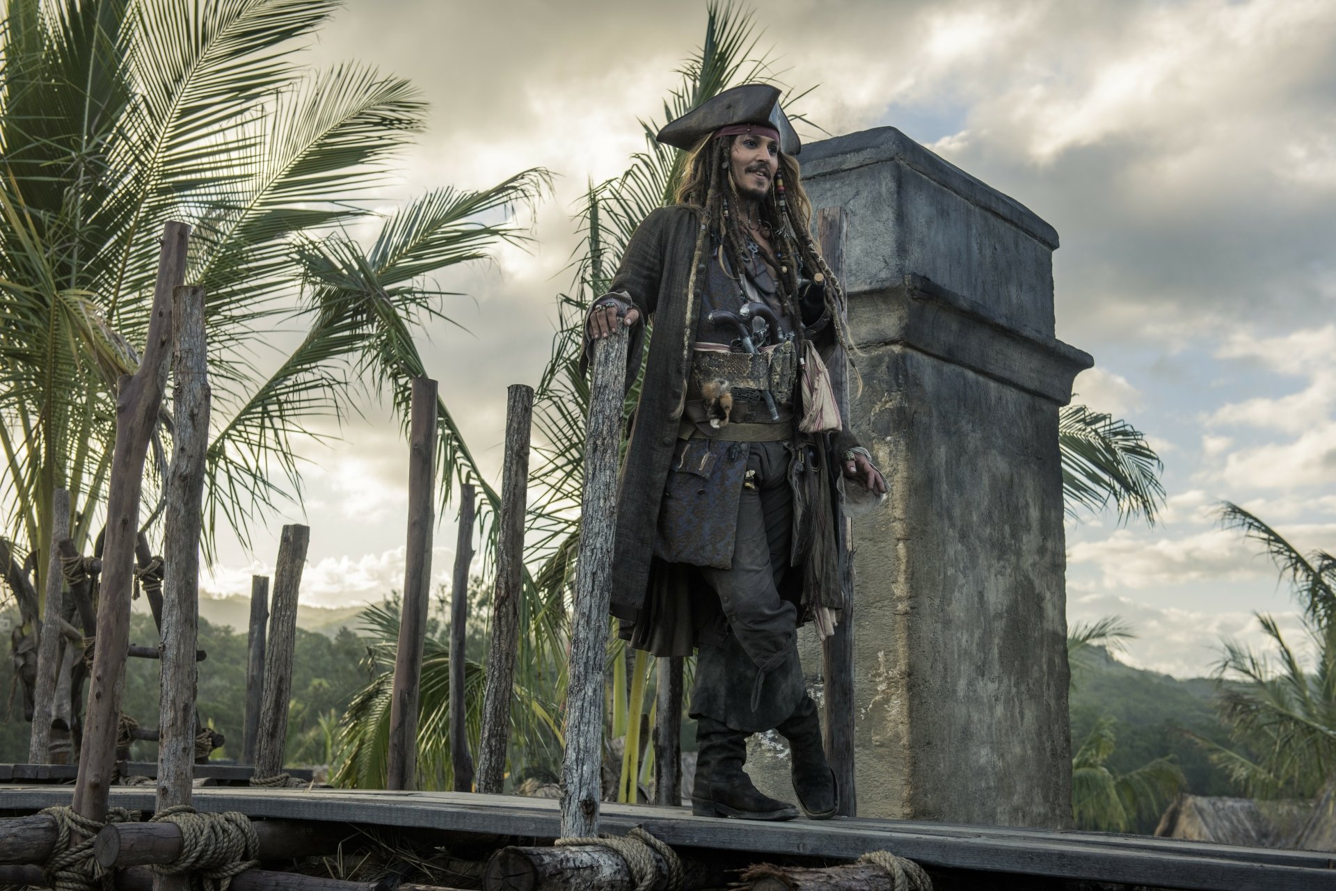 Jack Sparrow, portrayed by Johnny Depp in Pirates of the Caribbean: Dead Men Tell No Tales, stands on a tropical wooden bridge in this 4K Ultra HD movie wallpaper.