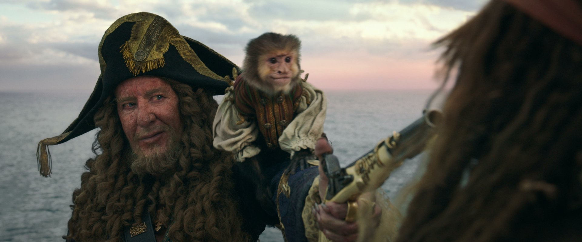 2K desktop wallpaper from Pirates of the Caribbean: Dead Men Tell No Tales showing a grizzled pirate captain with a small monkey on his shoulder against a sunset seascape.