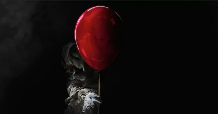 HD wallpaper featuring Pennywise the clown from the movie It (2017). He is partially obscured by a red balloon, creating a foreboding and eerie atmosphere. The background is dark and ominous.