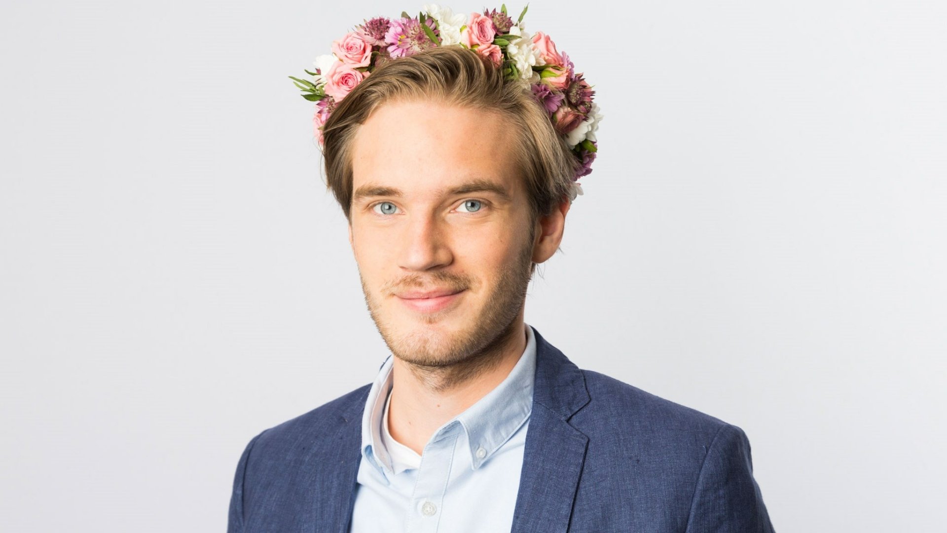 HD desktop wallpaper featuring a smiling man wearing a flower crown and a blue suit jacket, providing a simple and clean background.