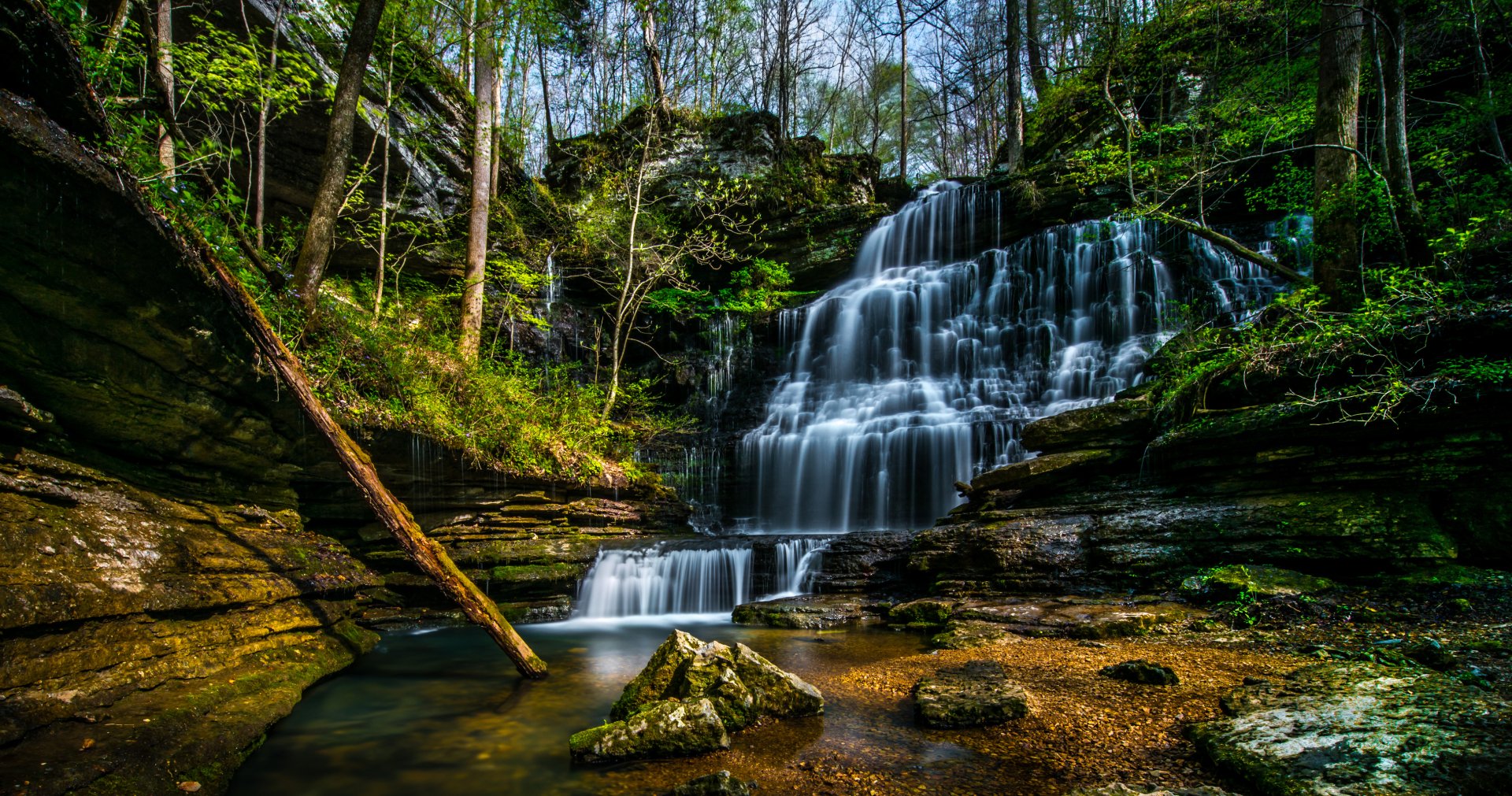 2K Quad HD PC desktop wallpaper and background — nature, waterfall: multi-tiered cascades flowing over mossy rock ledges into a tranquil pool amid sunlit forest.