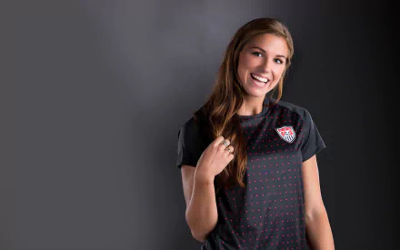 Alex Morgan smiles confidently while wearing a sports jersey against a dark background, creating an inspiring HD desktop wallpaper for sports enthusiasts.