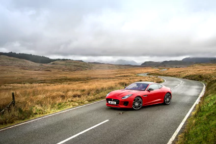 Red Jaguar F-Type sports car on a winding country road through rolling moorland under a cloudy sky — 4K Ultra HD PC desktop wallpaper background.