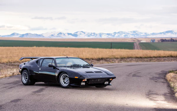 Black De Tomaso Pantera with hideaway headlights parked on a rural road, set against fields and distant mountains in this 4K Ultra HD PC desktop wallpaper.