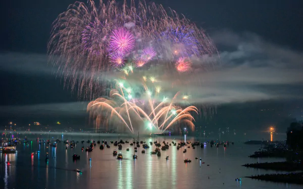 HD desktop wallpaper showcasing a colorful fireworks display over the sea at night in Vancouver, with boats scattered across the water.