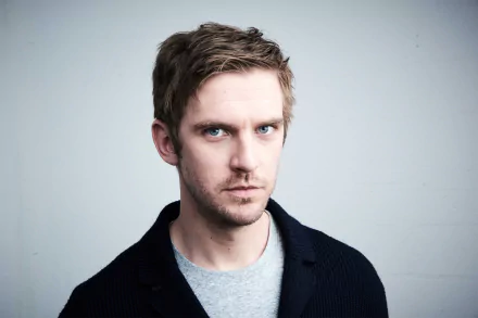 HD wallpaper of a man with intense gaze, wearing a dark jacket over a blue shirt, against a plain background.