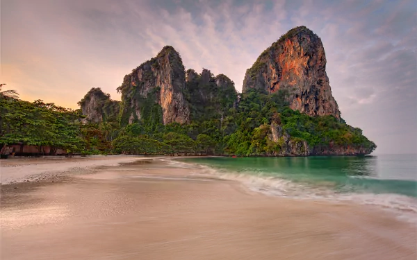 4K Ultra HD PC wallpaper of a tropical Thailand beach: soft sand, emerald water and dramatic limestone cliffs beneath a pastel dawn sky.
