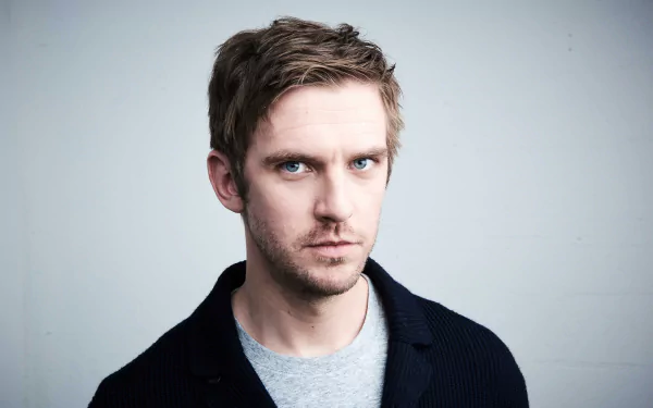 HD wallpaper of a man with intense gaze, wearing a dark jacket over a blue shirt, against a plain background.