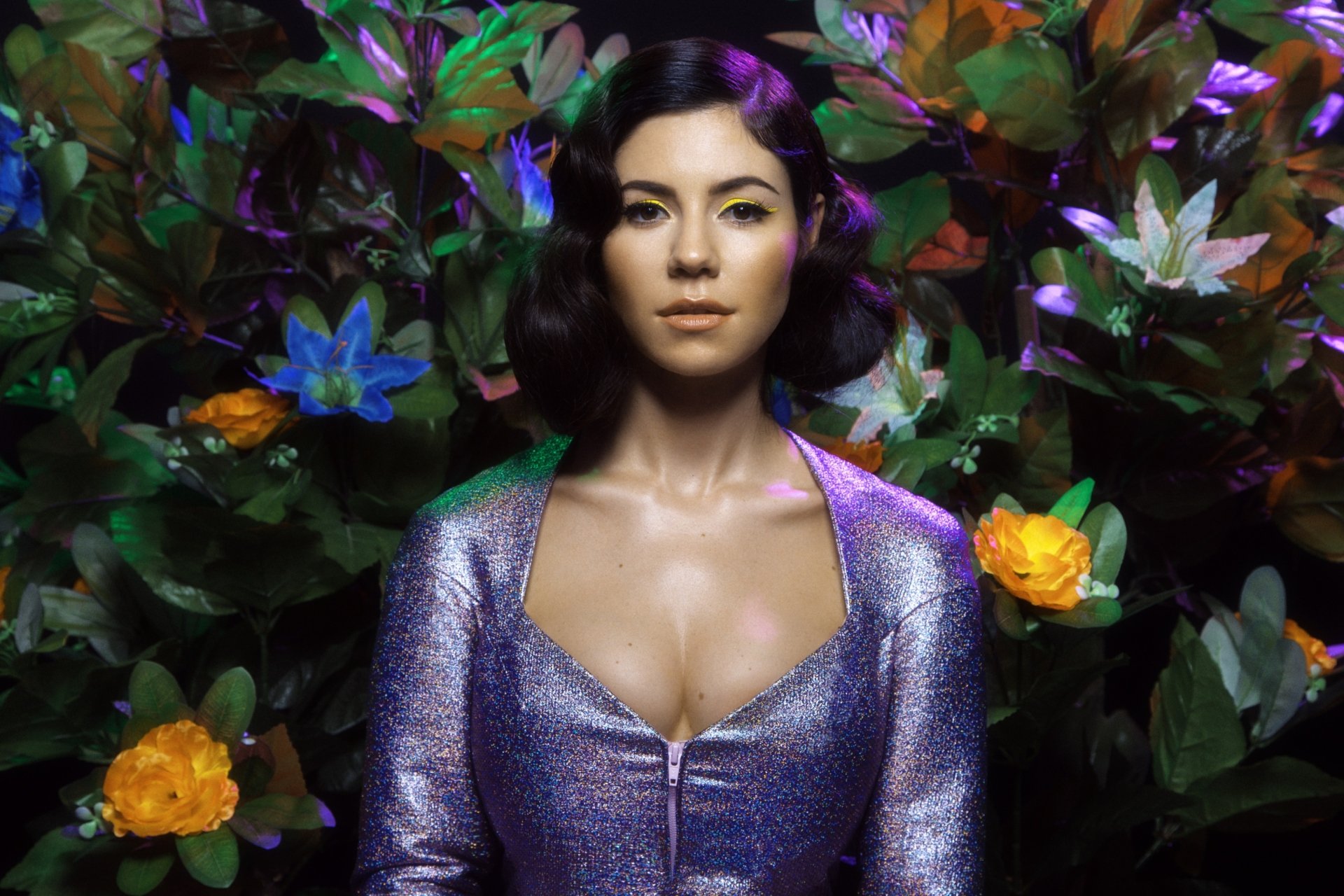 2K Quad HD PC wallpaper, music-themed: stylized female singer in a shimmering purple outfit amid lush foliage with yellow and blue flowers.