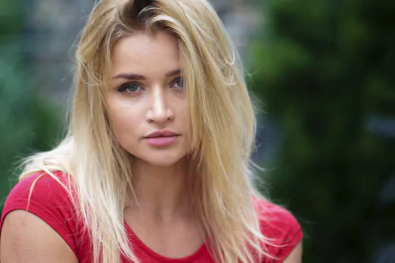 HD desktop wallpaper: close-up portrait of a blonde woman model with blue eyes, face framed by hair, shallow depth of field and a soft blurred green background.