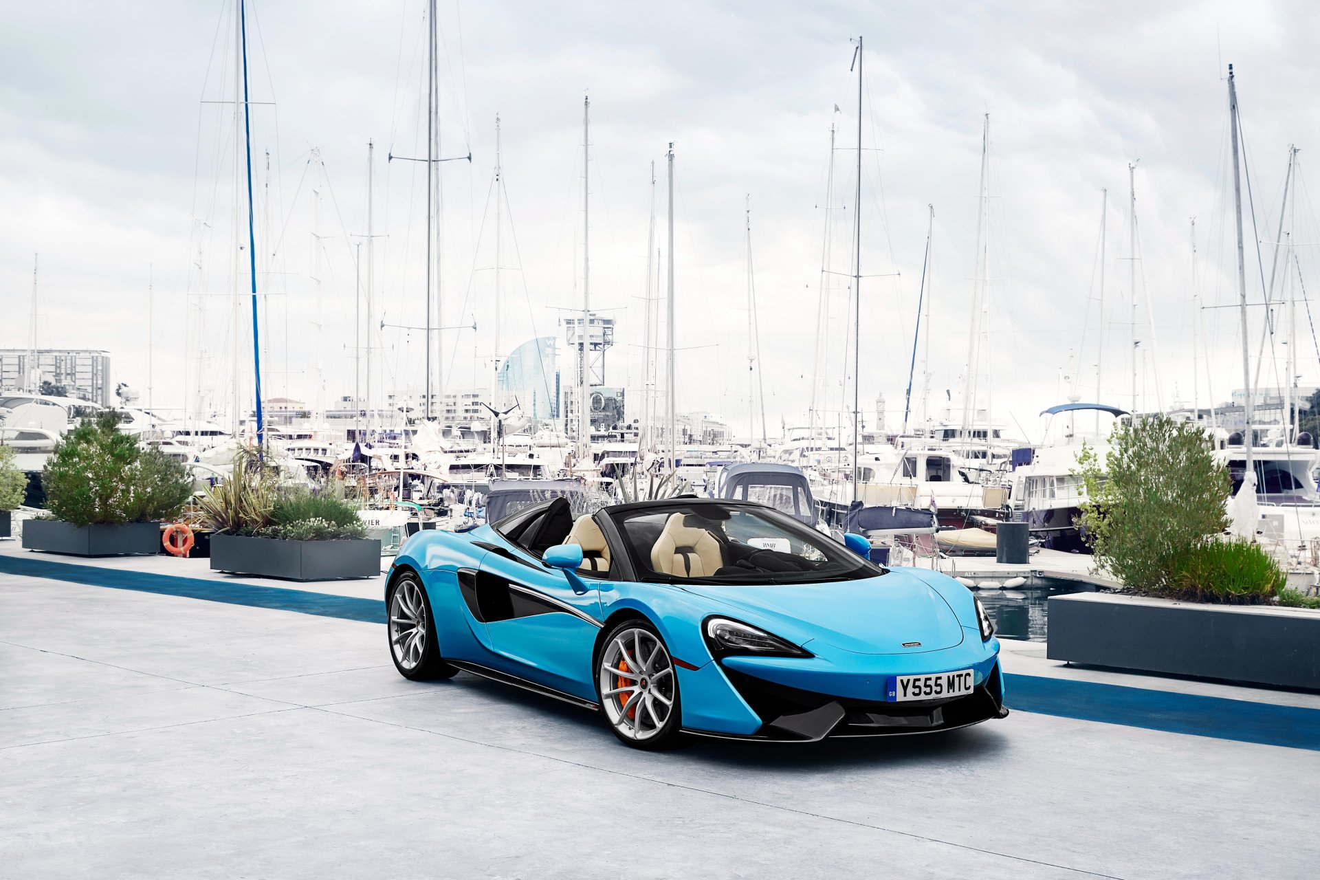 Blue McLaren 570S supercar parked on a harbor promenade with yachts behind — a sleek McLaren vehicle showcased as a 4K Ultra HD PC desktop wallpaper background.