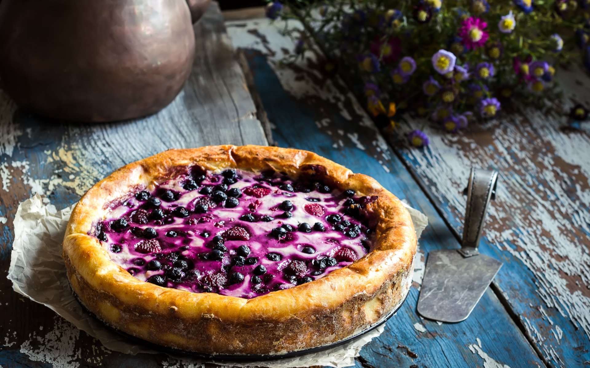 HD desktop wallpaper of a blueberry and raspberry pie on rustic wooden table, accompanied by a vintage pie server and a vase of wildflowers.