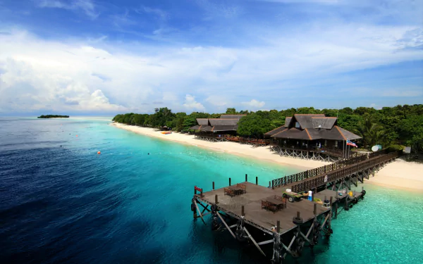 HD desktop wallpaper of a tropical beach resort featuring overwater bungalows and a wooden pier extending into the clear blue ocean under a partly cloudy sky.