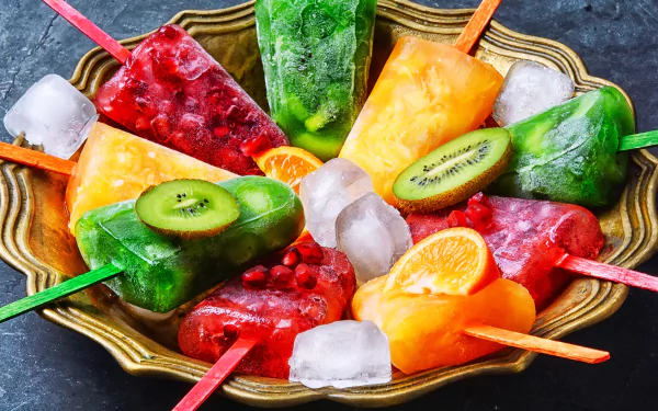 Colorful ice cream popsicles with slices of fruits arranged in a bowl with ice cubes. HD desktop wallpaper and background featuring vibrant sweets and food.
