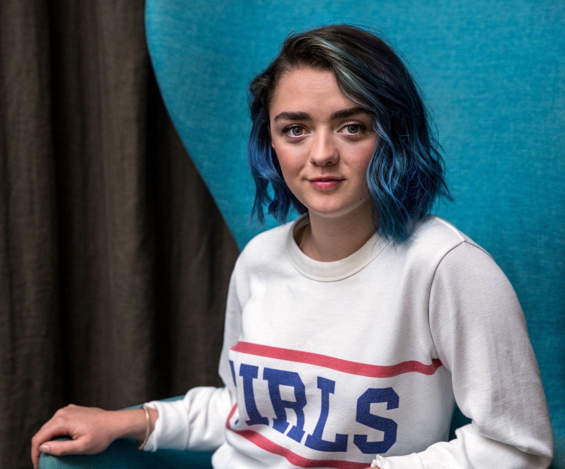 HD desktop wallpaper featuring celebrity Maisie Williams with blue hair, wearing a white sweatshirt, against a blue and dark brown background.