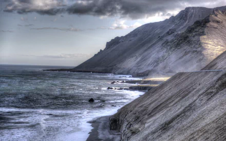 2K Quad HD PC desktop wallpaper/background: rugged mountain coastline meeting the ocean at low tide under moody clouds, panoramic horizon and rocky beach landscape.