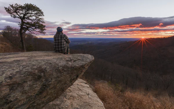 Sunrise over Shenandoah National Park in Virginia, USA, with a person sitting on a rock ledge overlooking the expansive morning landscape.
