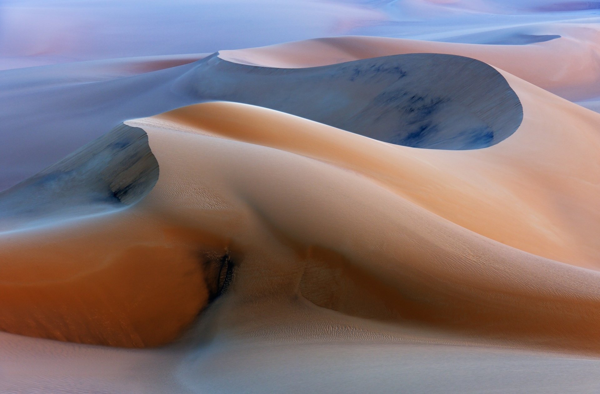 A stunning HD wallpaper showcasing the serene beauty of sand dunes in a desert landscape, featuring smooth curves and gentle hues of orange and blue.