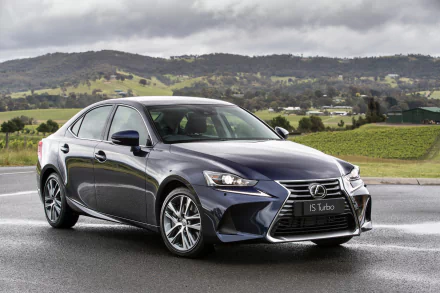 Sleek Lexus IS sedan parked on wet pavement with green hills and cloudy sky — car/vehicle desktop background (2K Quad HD PC wallpaper).