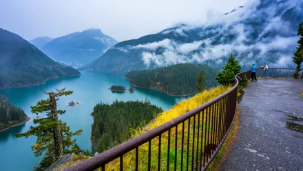 Fog-shrouded mountains and evergreen forest surrounding turquoise Diablo Lake, viewed from a railing overlook — HD PC desktop wallpaper and background landscape photo.