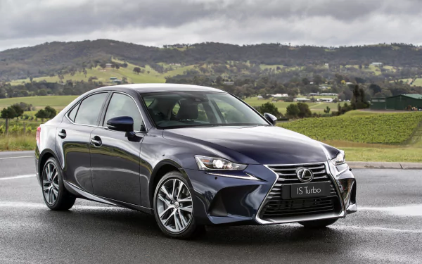 Sleek Lexus IS sedan parked on wet pavement with green hills and cloudy sky — car/vehicle desktop background (2K Quad HD PC wallpaper).