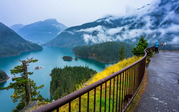Fog-shrouded mountains and evergreen forest surrounding turquoise Diablo Lake, viewed from a railing overlook — HD PC desktop wallpaper and background landscape photo.