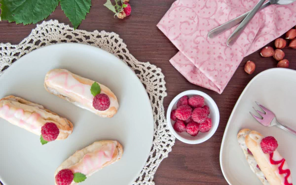 HD PC desktop wallpaper background — still life of raspberry éclairs on white plates with doily, bowl of raspberries, pink napkin and scattered hazelnuts; pastry dessert close-up.